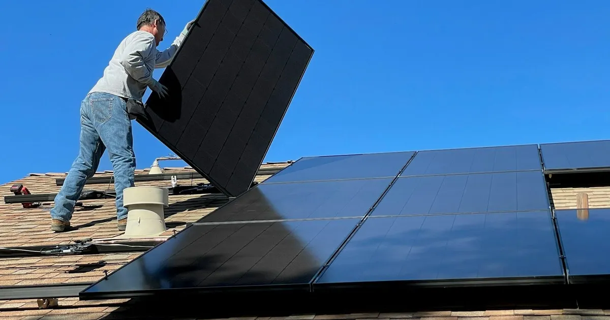 Installateur tilt een zwart zonnepaneel op een schuin dak onder een strakblauwe lucht
